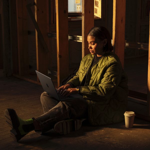 Eine Person sitzt mit einem Laptop auf dem Schoß am Boden eines Raumes, der gerade renoviert wird.