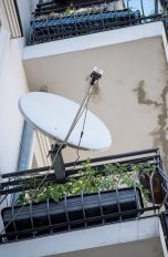 Eine Satellitenschüssel ist auf einem Balkon an einem Mehrfamilienhaus befestigt.