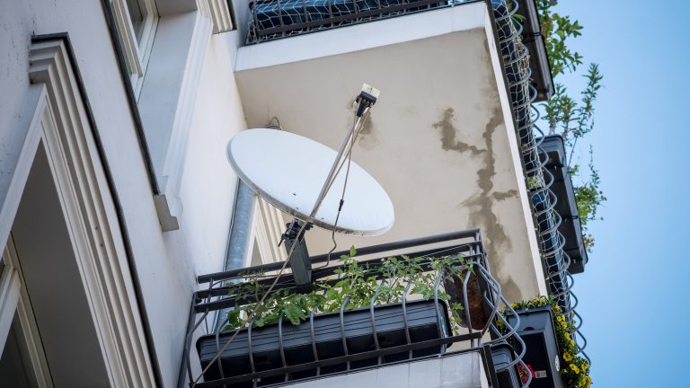 Eine Satellitenschüssel ist auf einem Balkon an einem Mehrfamilienhaus befestigt.