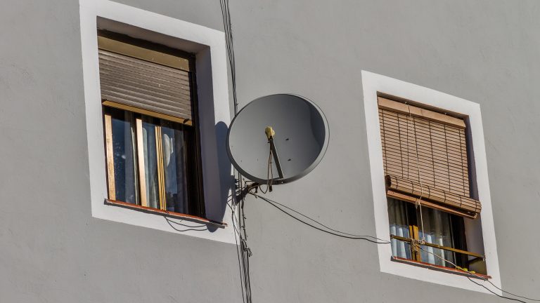 Eine Satellitenschüssel ist an einer Wandhalterung an einer Hauswand befestigt.