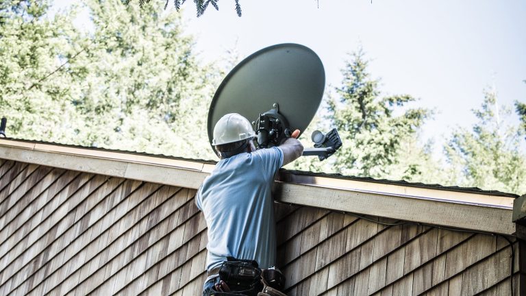 Eine Person mit Helm richtet eine Satellitenschüssel auf einem Dach aus.