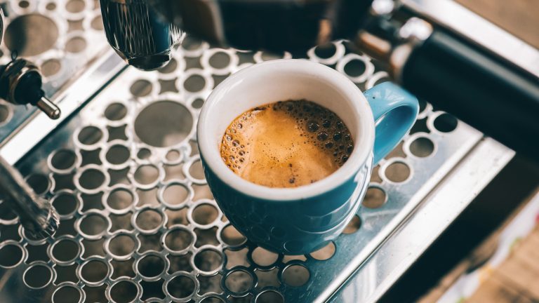 Nahaufnahme einer blauen Espresso-Tasse auf dem Gitter einer Siebträgermaschine.