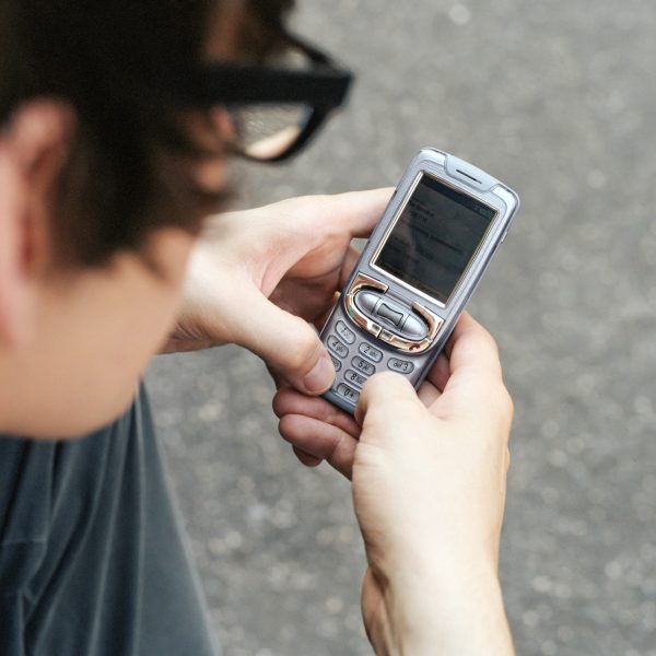 Eine Person hält ein altes Mobiltelefon mit Tasten in der Hand und schreibt darauf eine Nachricht.