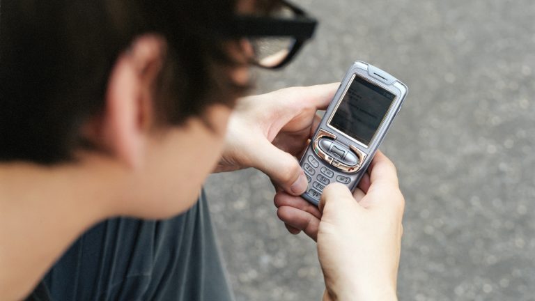 Eine Person hält ein altes Mobiltelefon mit Tasten in der Hand und schreibt darauf eine Nachricht.