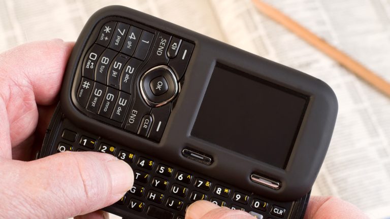 Eine Person hält ein altes Mobiltelefon mit einer QWERTY-Tastatur zum herausschieben in den Händen.