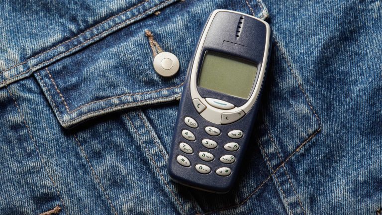 Ein Nokia 3310 liegt ausgeschaltet auf einer Jeansjacke.