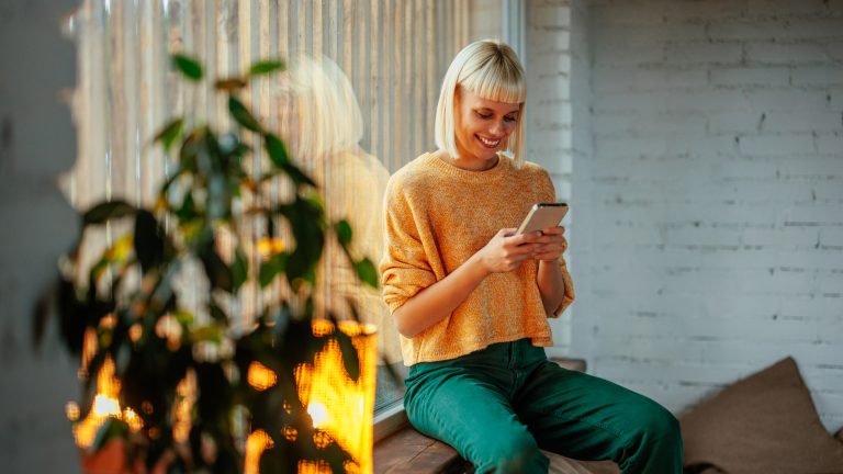 Eine Person sitzt neben einer Lampe und schaut auf ihr Smartphone.