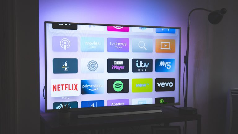 Ein Fernseher steht in einem dunklen Wohnzimmer. Der Bildschirm zeigt verschiedene Apps, zum Beispiel von Netflix, Prime Video und Vevo.