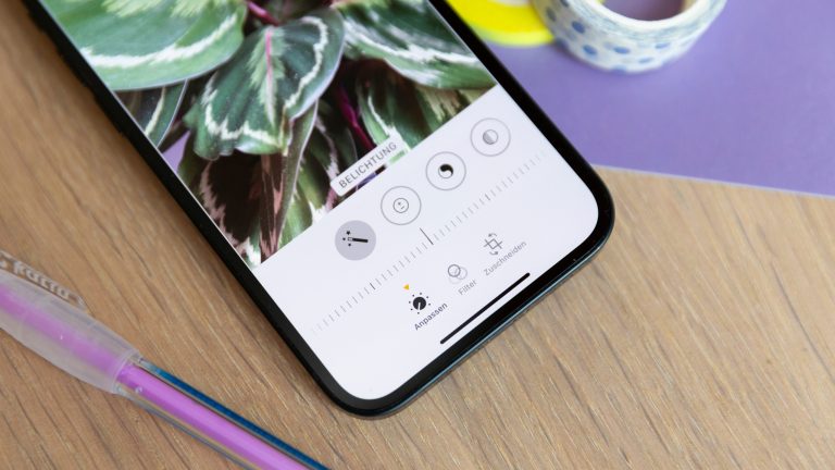 Ein iPhone liegt auf einem Holztisch. Die Fotos-App ist im Bearbeitungsmodus geöffnet und der Regler der Belichtung steht in der Mitte.