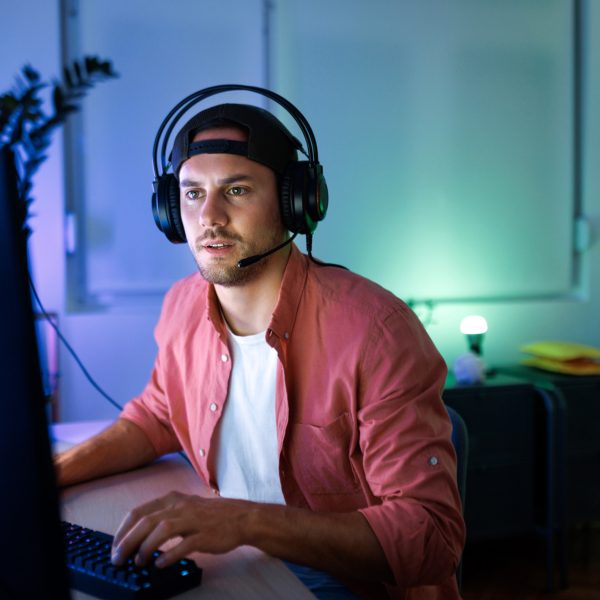 Eine Person sitzt mit einem Headset vor einem PC – Hände an der Maus und der Tastatur. Der Raum ist blau und grün beleuchtet.