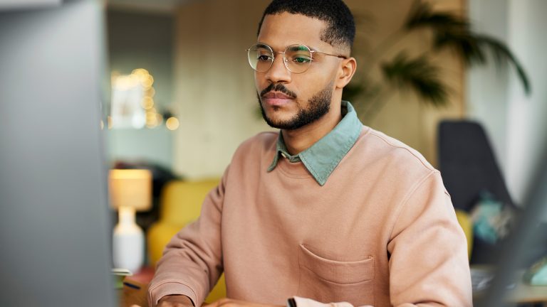 Eine Person sitzt im Business-Outfit an ihrem Rechner und tippt etwas auf der Tastatur.