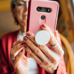 Eine Person hält ein Smartphone mithilfe eines PopSockets in der Hand. Der Fokus der Aufnahme liegt auf der Rückseite des Smartphones sowie den Händen der Person.