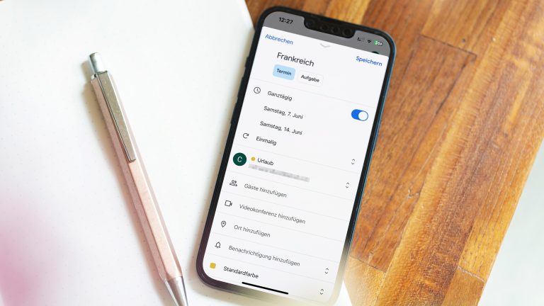 Ein iPhone liegt auf einem Notizblock. Auf dem Display ist ein erstellter Eintrag im Google Kalender für einen Urlaub zu sehen.