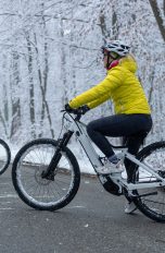 Zwei winterlich gekleidete Personen machen mit ihren E-Bikes Halt auf einer vereisten Waldstraße.