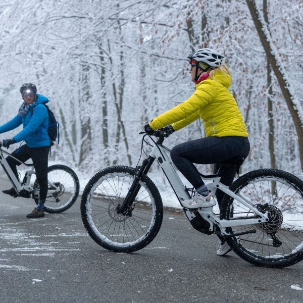 Zwei winterlich gekleidete Personen machen mit ihren E-Bikes Halt auf einer vereisten Waldstraße.