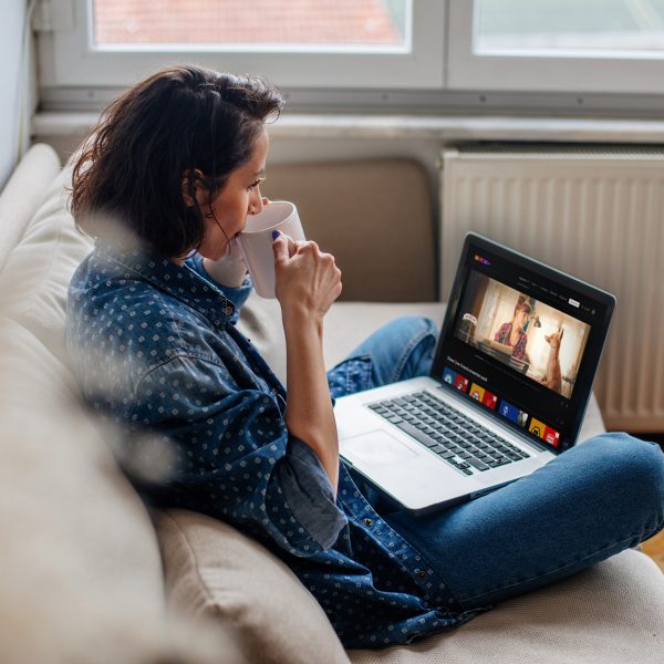 Eine Person sitzt mit einer Tasse auf dem Sofa vor einem Laptop und nutzt RTL+.