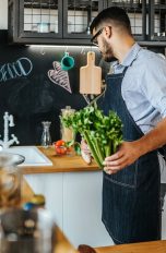 Eine Person steht in einer Küche mit Staudensellerie in der Hand.