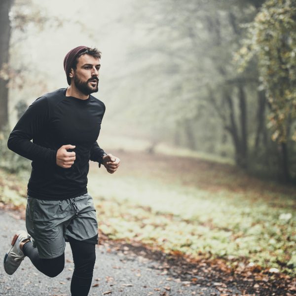 Ein Mensch joggt in Sportklamotten auf einer Straße in einem diesigen Wald.